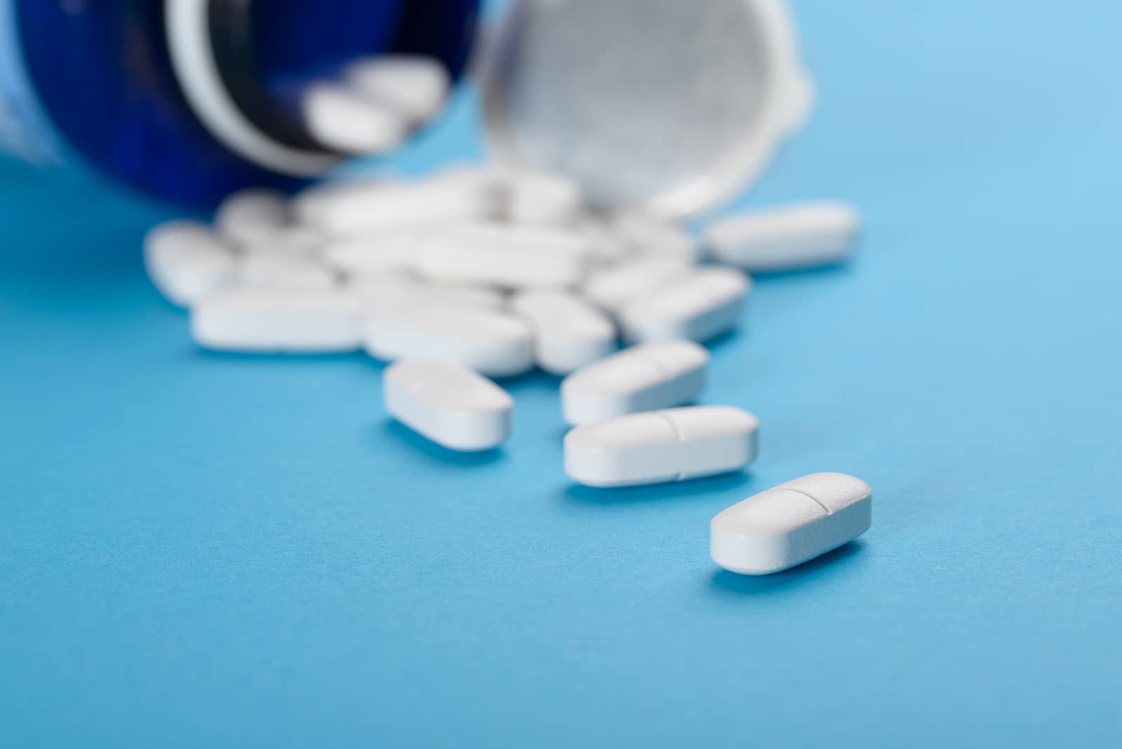 Pills Spilling Out Of A Prescription Bottle Over Blue Background