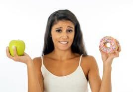 Beautiful young woman tempted having to make choice between apple and doughnut in healthy unhealthy food, detox eating, calories and diet concept.