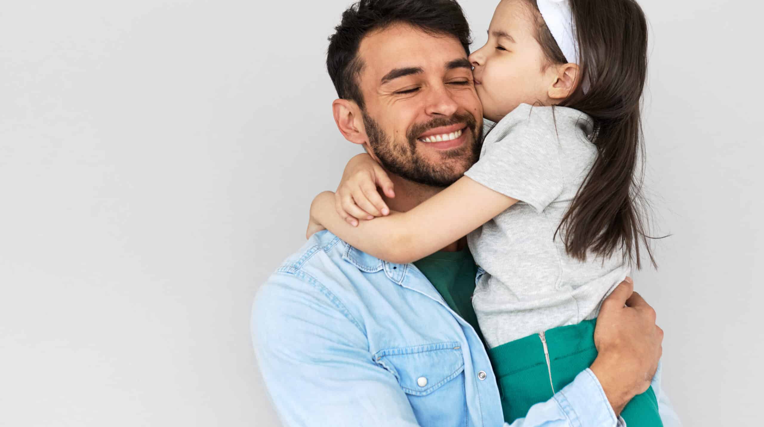 Indoor image of happy father smiling broadly hold embrace his cute daughter kissing on the cheek. Loving daddy and his little girl cuddling and enjoying time together. Childhood and fatherhood concept