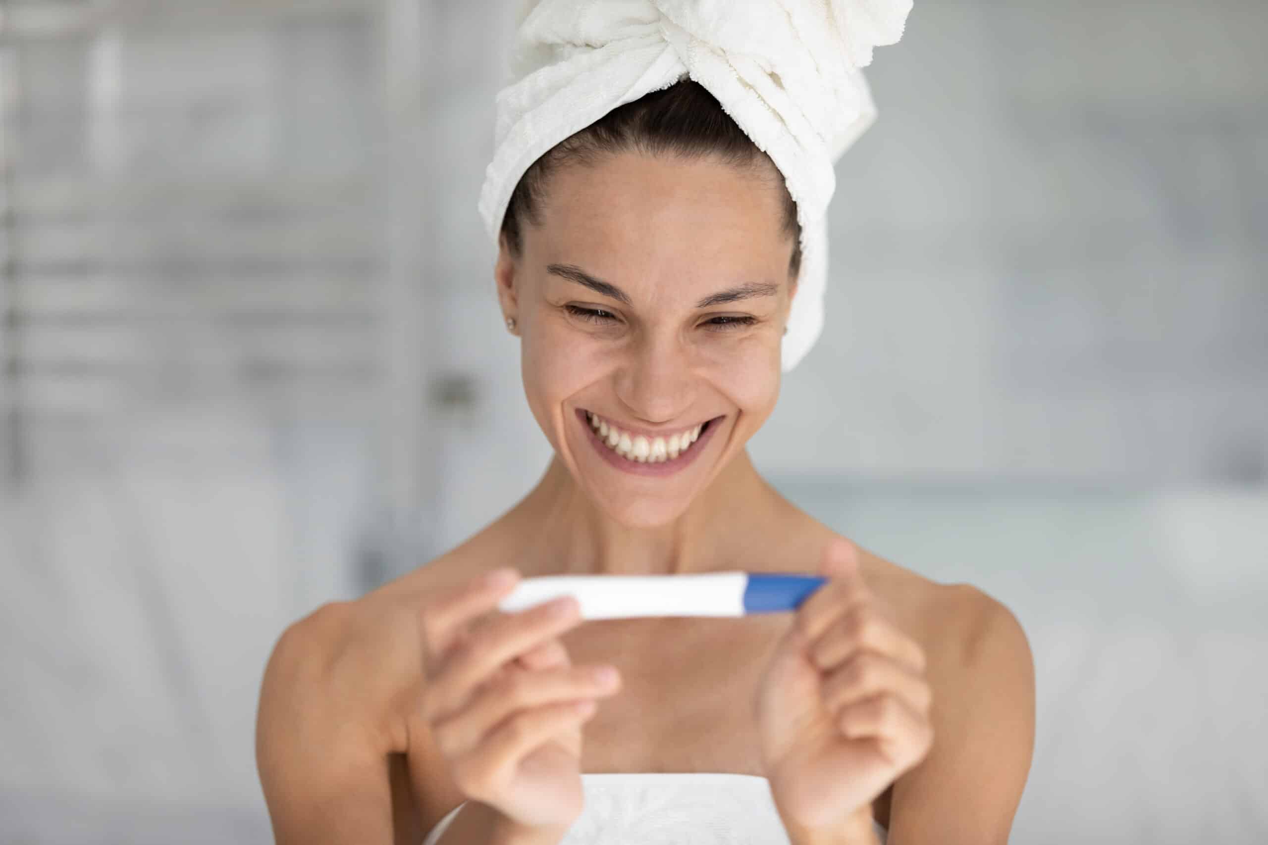 Happy beautiful young mixed race woman looking at pregnancy test.